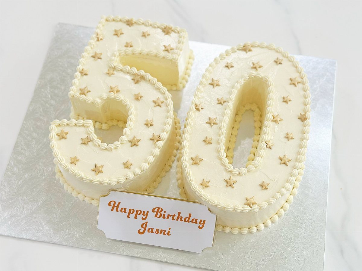 A white number 50 shaped cake decorated with small gold stars on a silver board.
