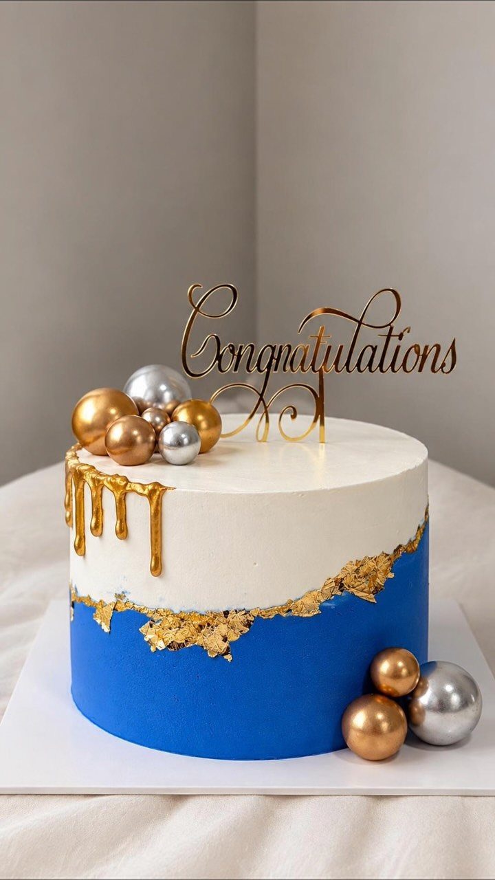A white and blue cake featuring a gold ganache drip and metallic decorative spheres.