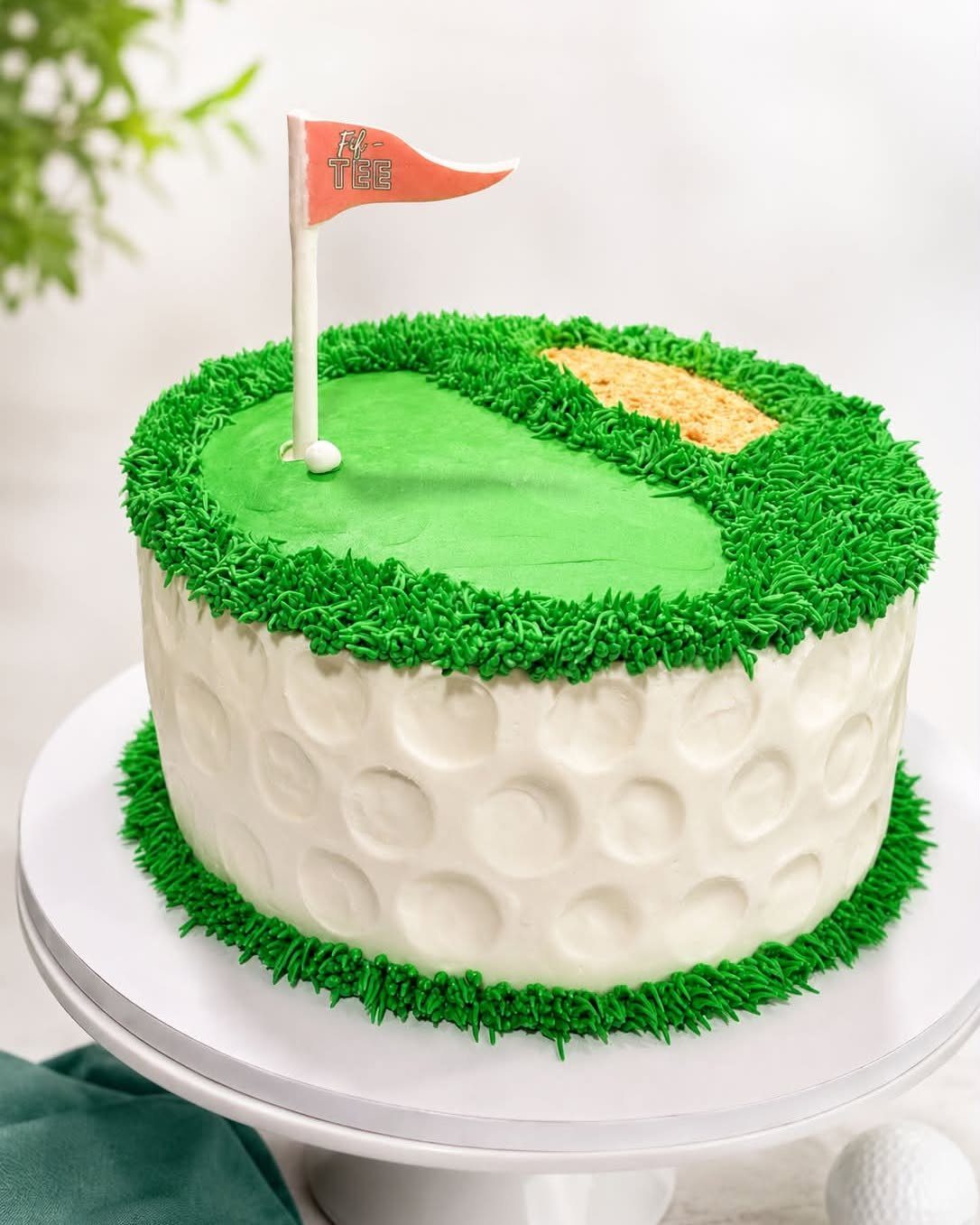 A golf themed cake with white dimpled frosting and a green grass top with a red flag.
