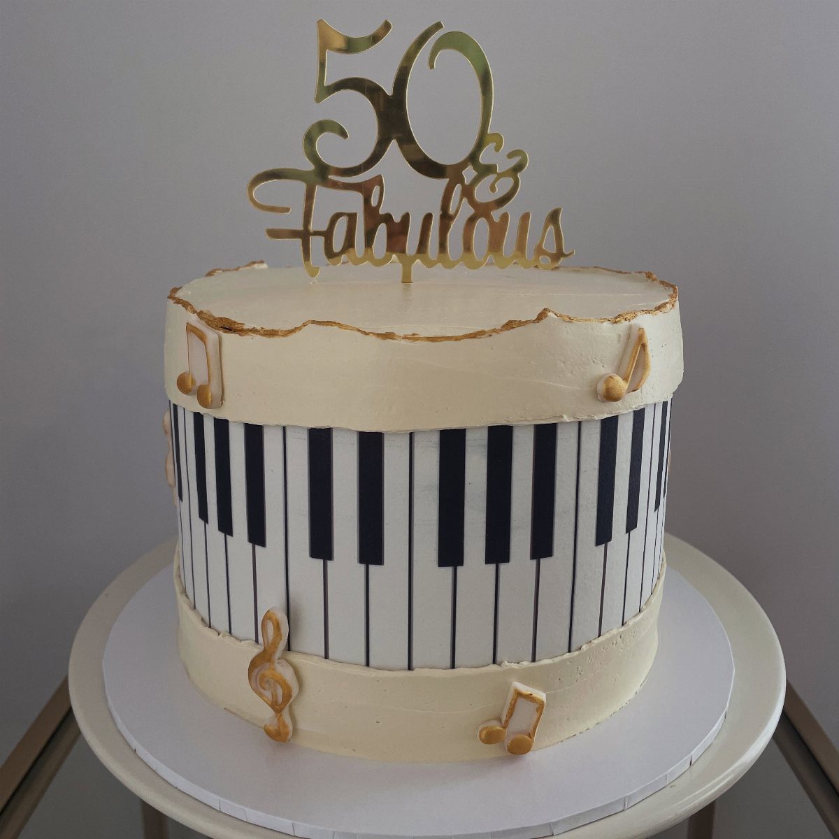 Cream cake with piano key decorations, gold musical notes, and a 50 & Fabulous topper.