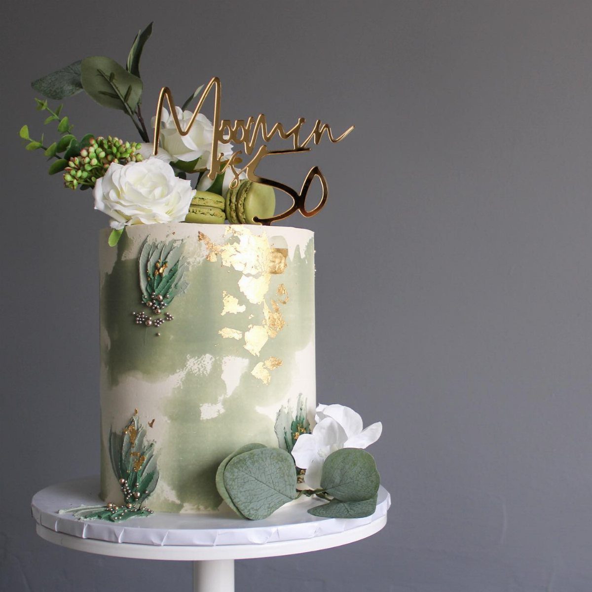 Sage green watercolor cake with gold leaf, white roses, and a gold 'Mommy 50' topper.