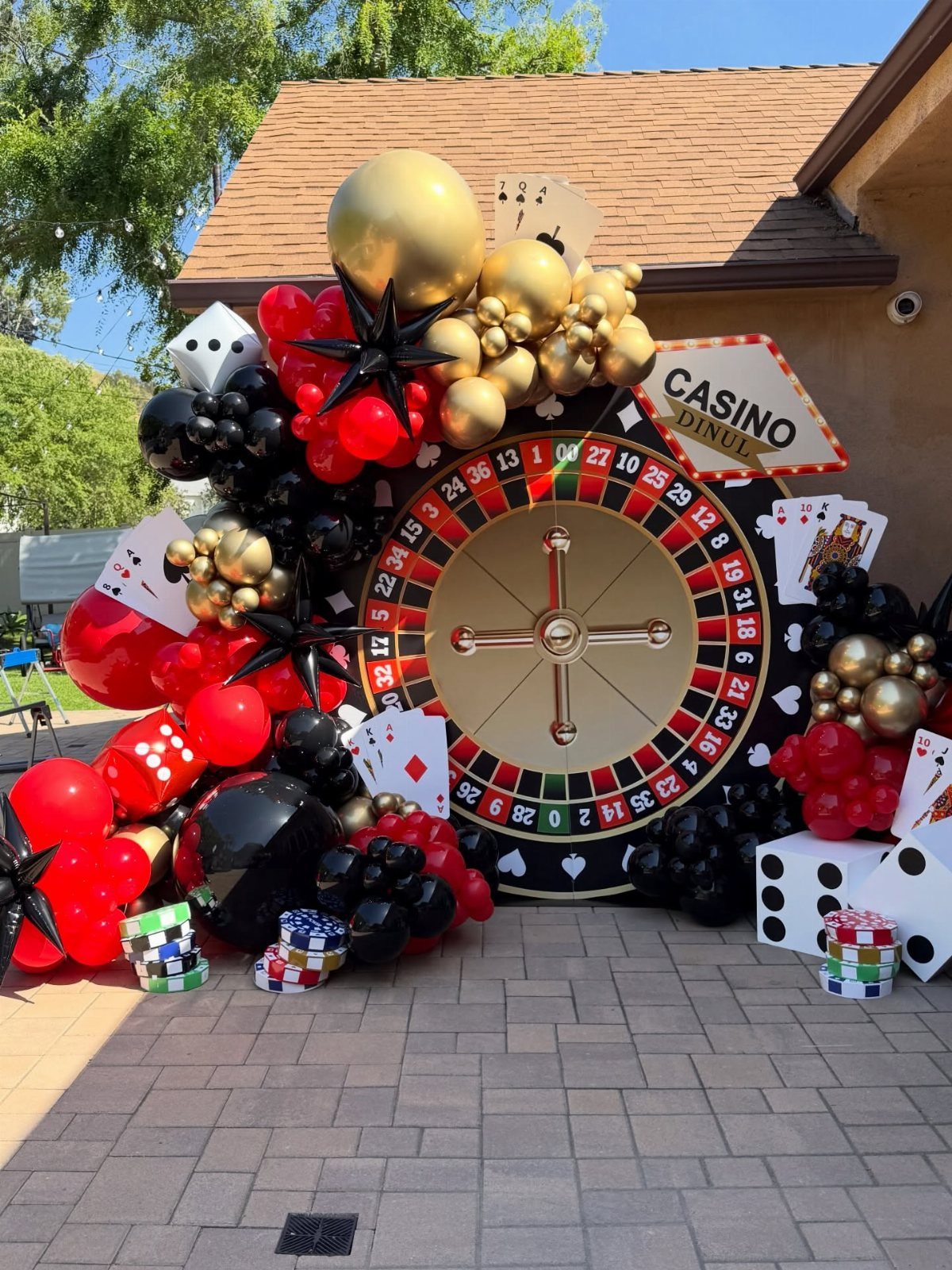 Red, black, and gold balloon arch surrounding a large roulette wheel and casino themed decorations.