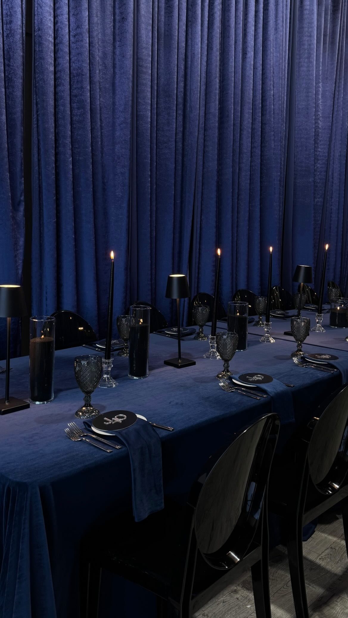 A formal dining table set with navy blue linens, black candles, and dark glassware.