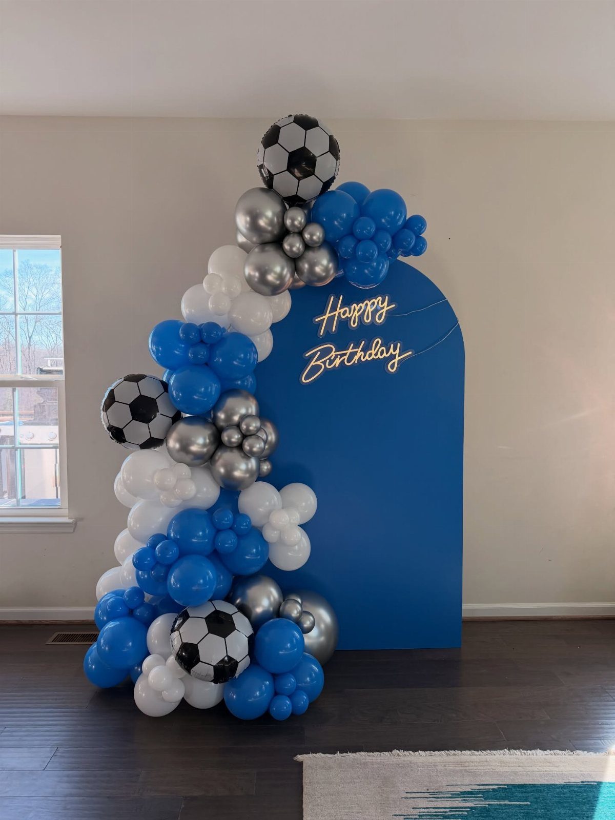 Blue birthday backdrop with soccer ball balloons and a blue, white, and silver balloon garland.