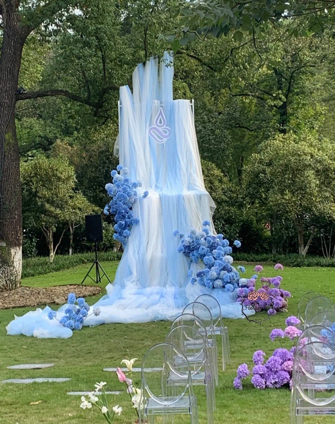 A large blue and white fabric installation resembling a waterfall decorated with blue hydrangeas on a lawn.