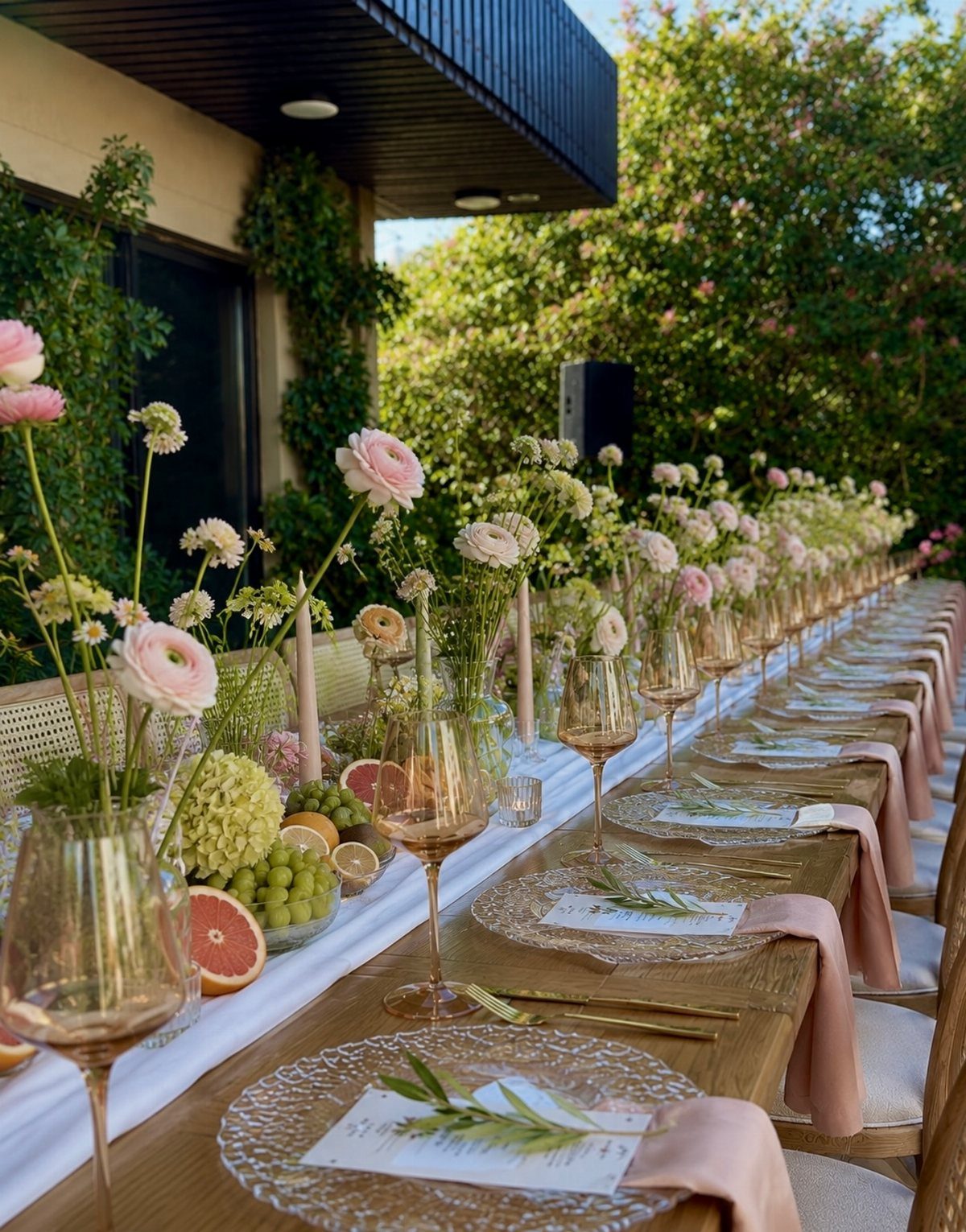An elegant outdoor dining table set with pink flowers, glassware, and fine dinnerware.
