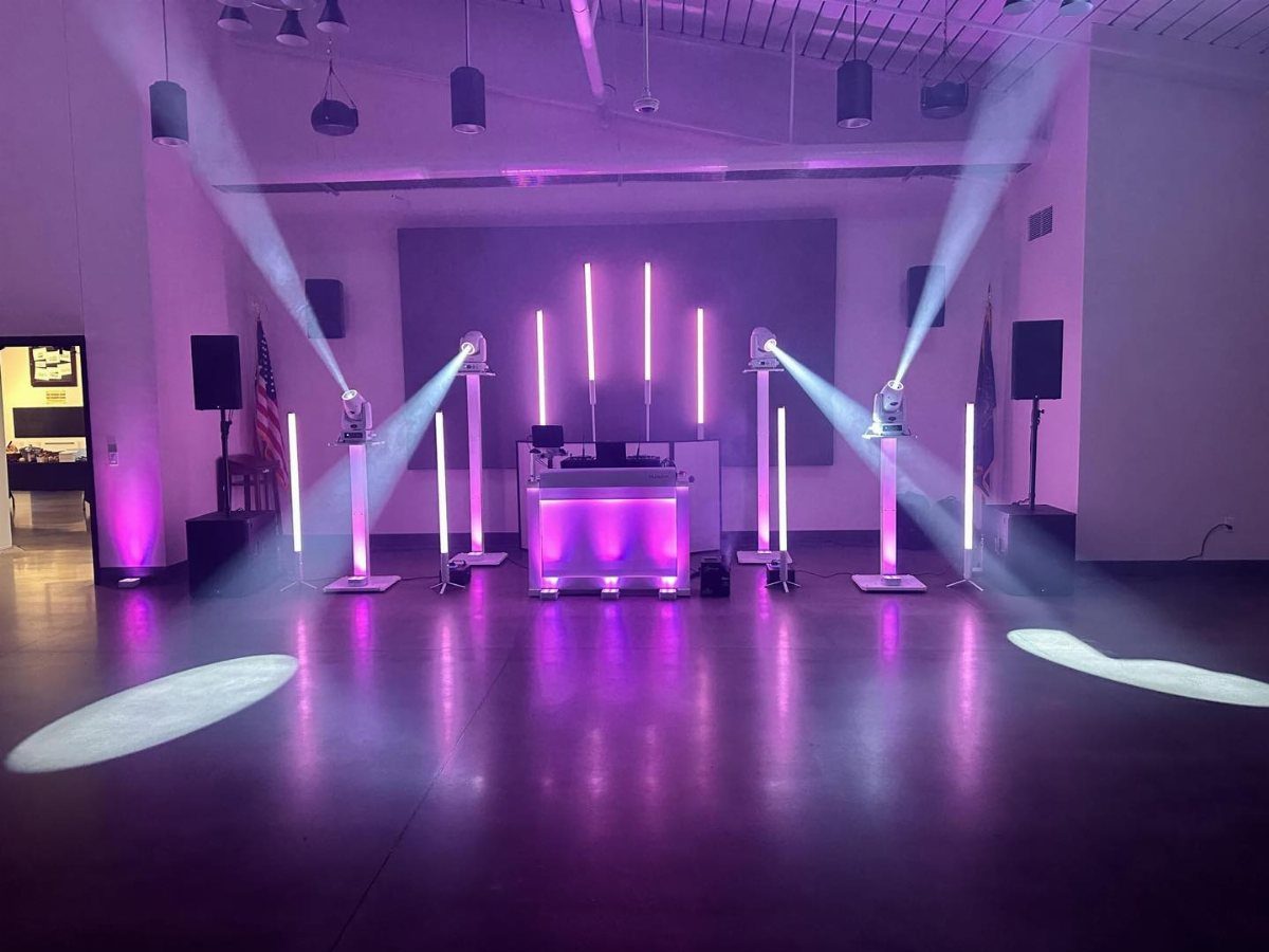 Purple and white stage lights and vertical light tubes illuminating a large event hall.