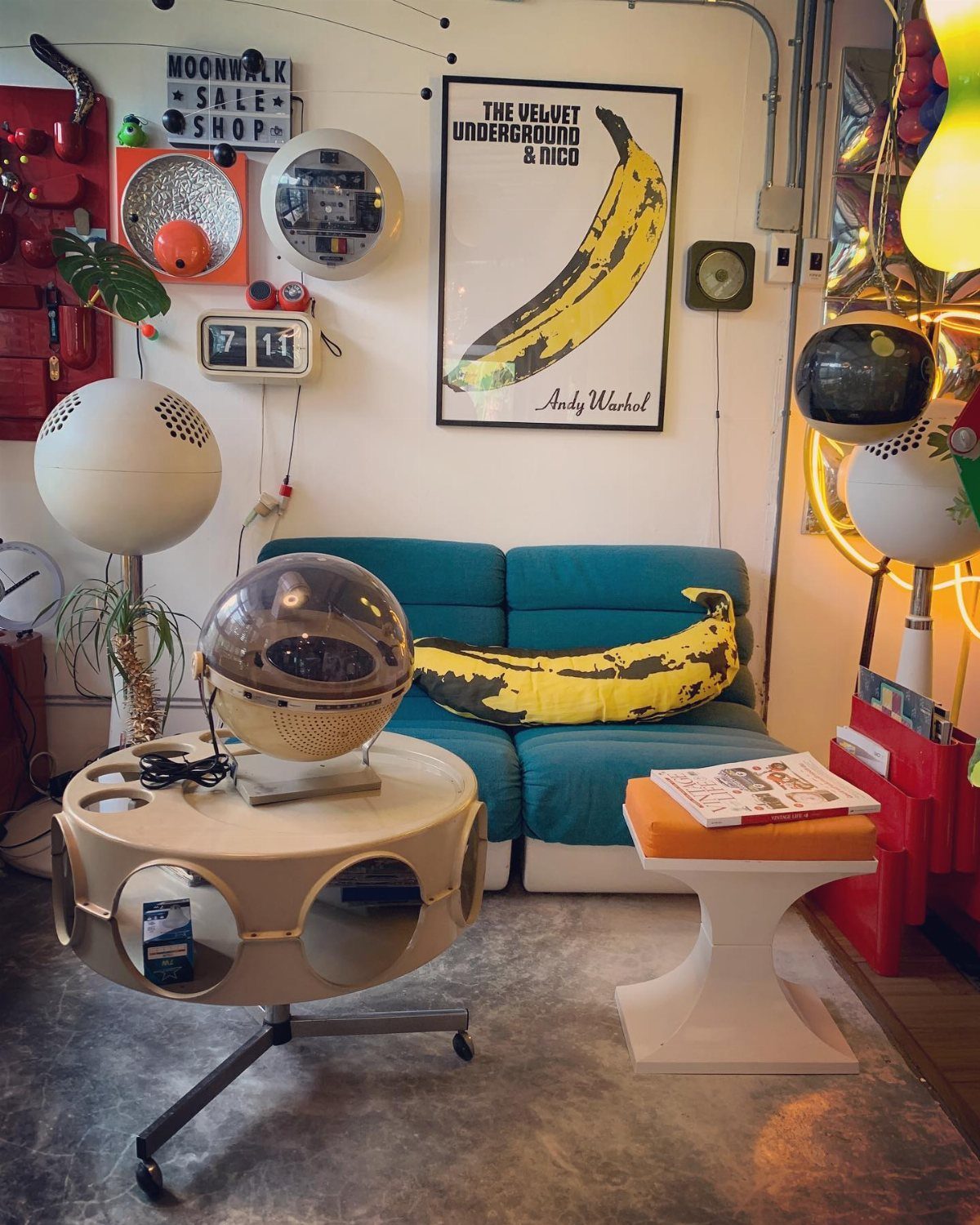 Retro room with teal sofa, banana print poster, and spherical white lamps.