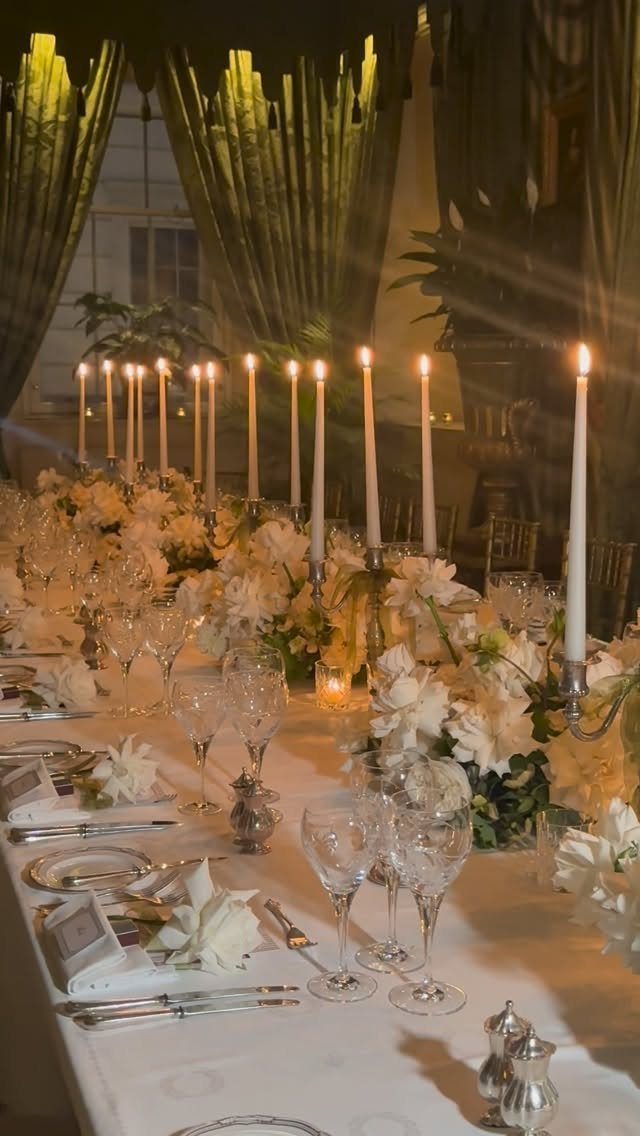 A long, elegant dinner table decorated with white flowers and many tall lit taper candles.