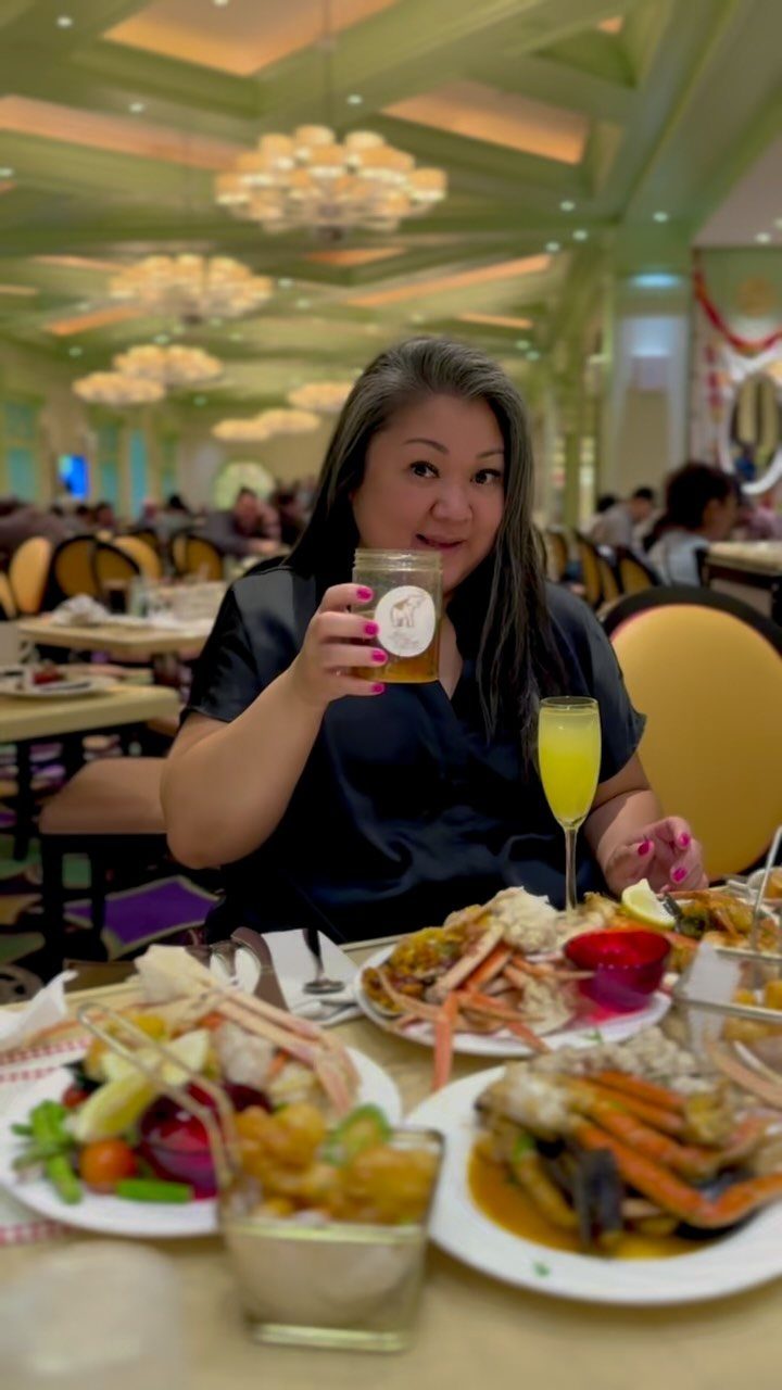 A woman smiling while holding a drink in front of plates of seafood.