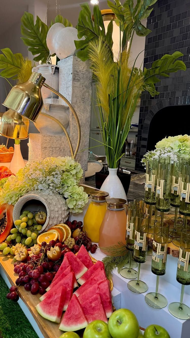 A colorful brunch buffet spread with sliced watermelon, grapes, citrus fruits, juices, and sparkling drinks.