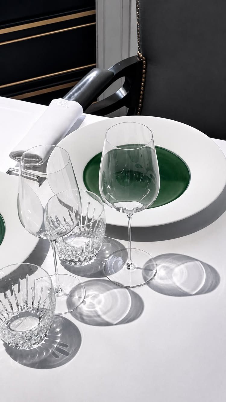 Elegant white and green plates with crystal wine glasses set on a white tablecloth.