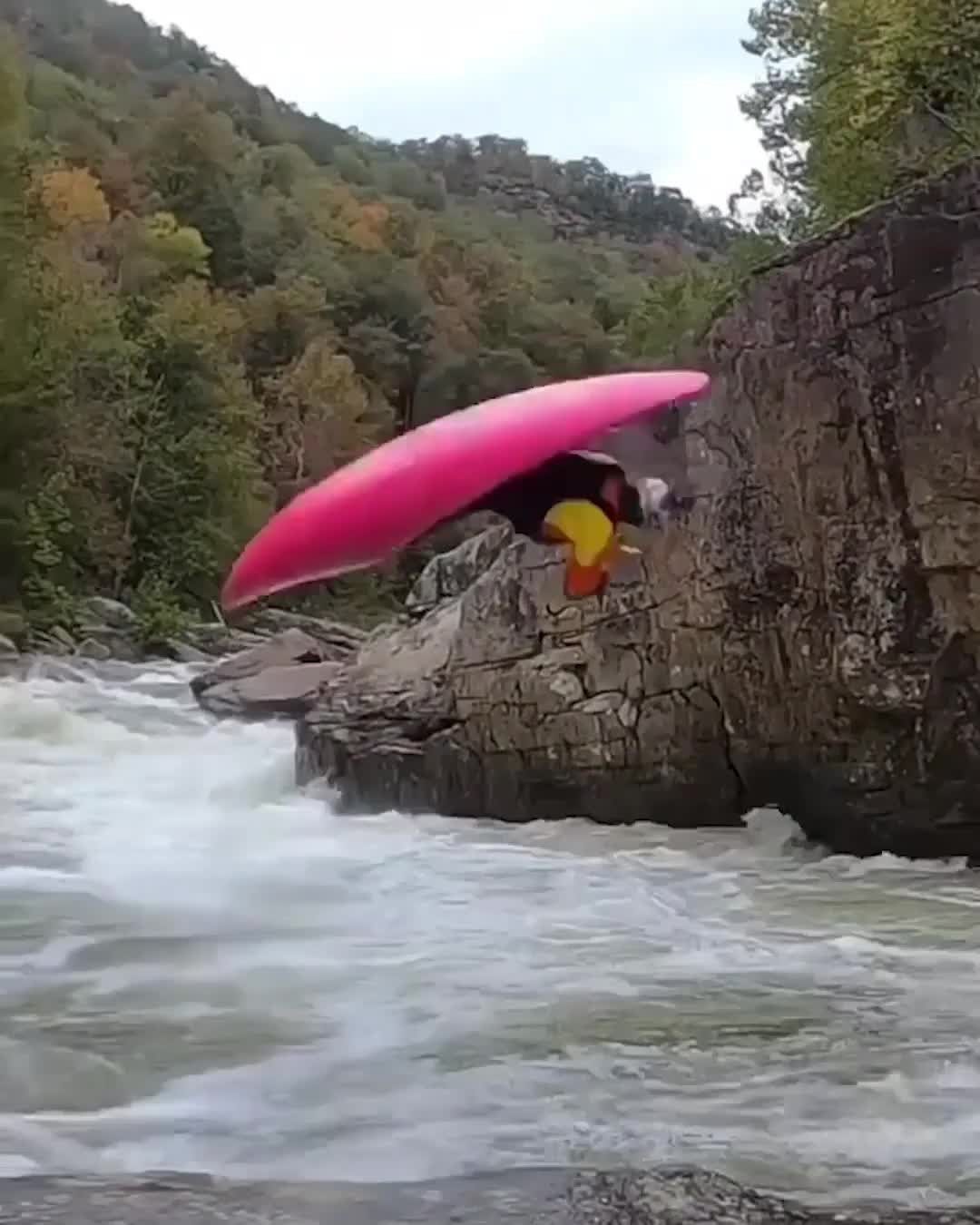 A person in a pink kayak performing a stunt over rocky river rapids.