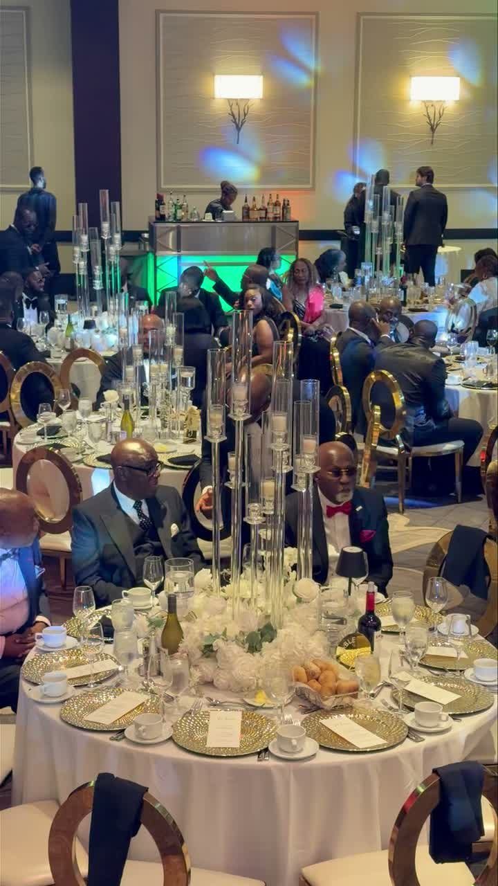 Formal banquet tables with gold chargers and tall glass centerpieces in a decorated ballroom.
