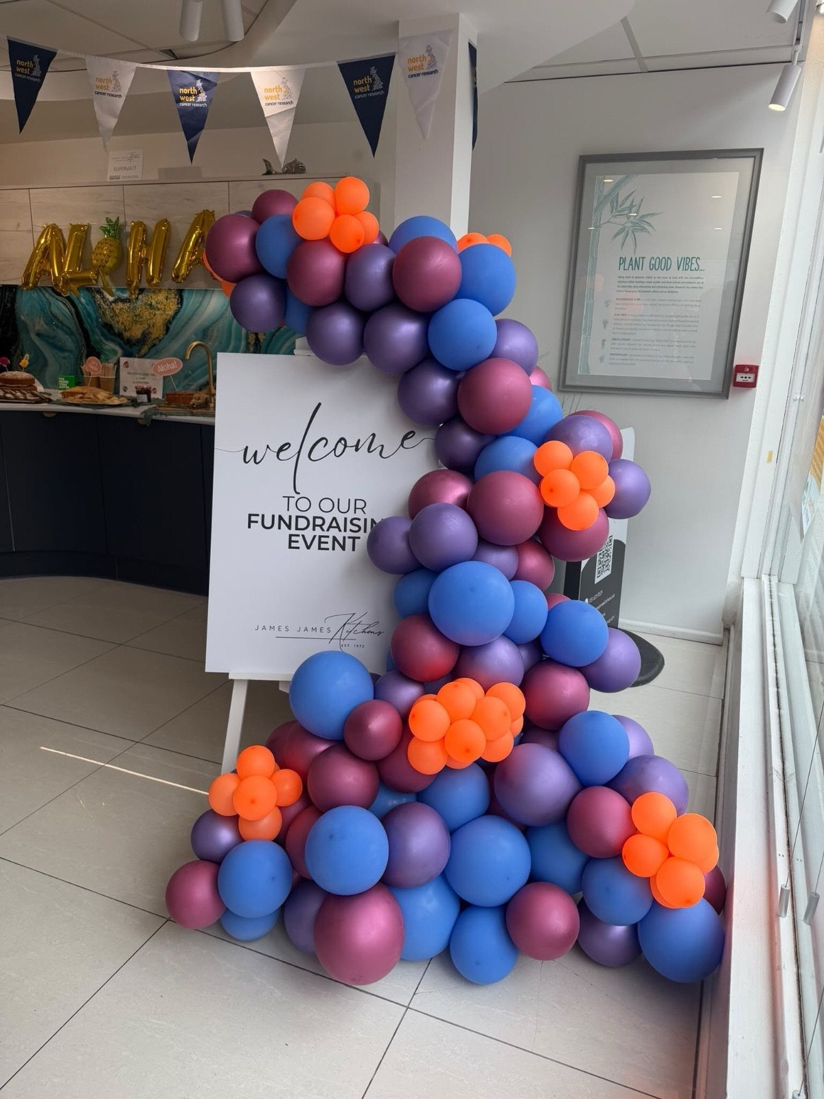 A colorful balloon arch in purple, blue, and orange next to a fundraising event sign.