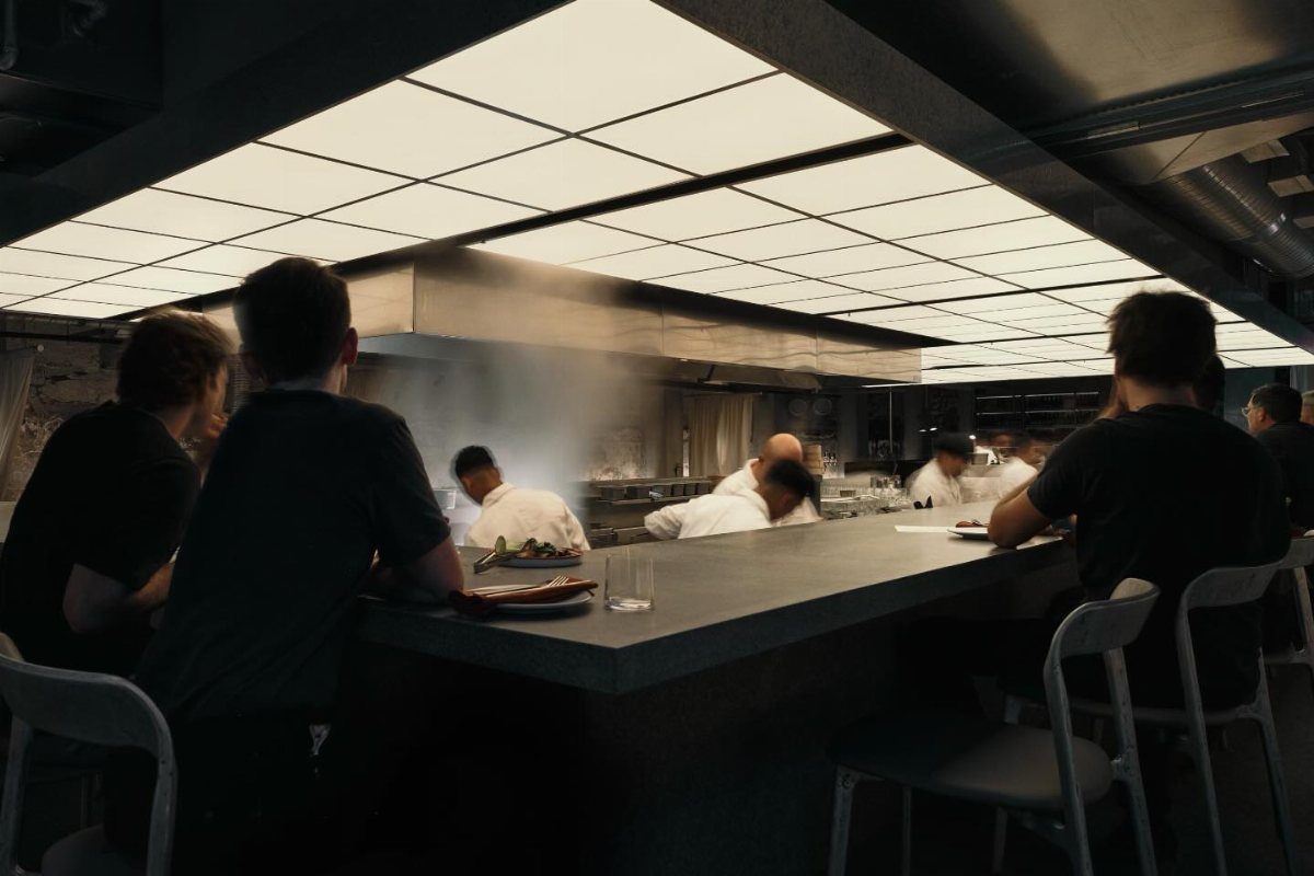 People sitting at a counter watching chefs cook in a professional kitchen.