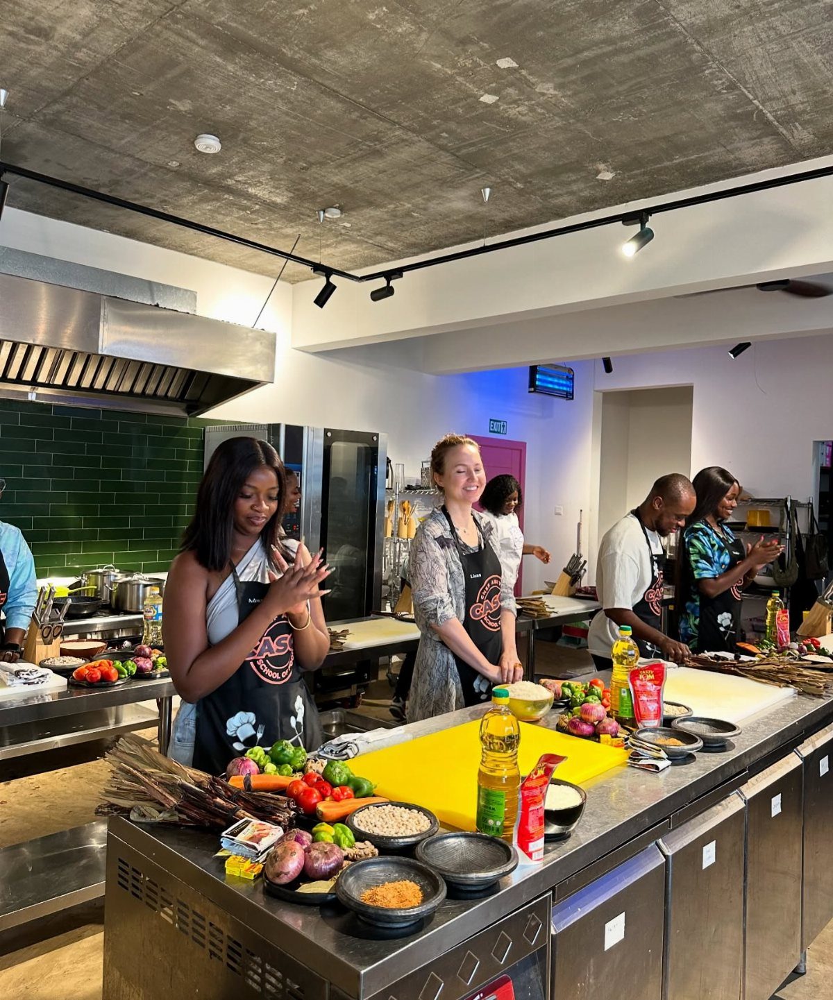 People in black aprons preparing to cook in a modern kitchen with fresh vegetables.