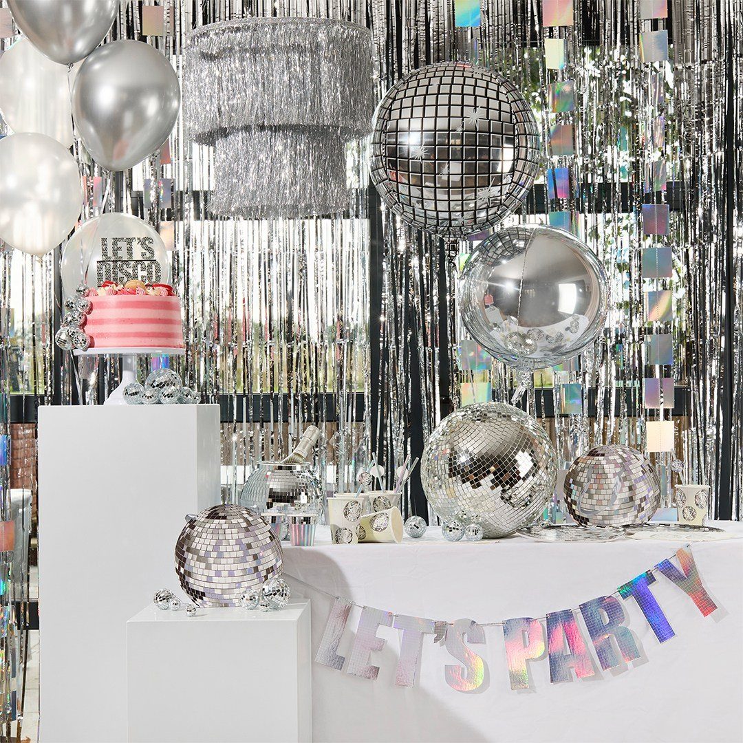 Silver disco balls, balloons, and tinsel decorations surrounding a pink cake and party banner.