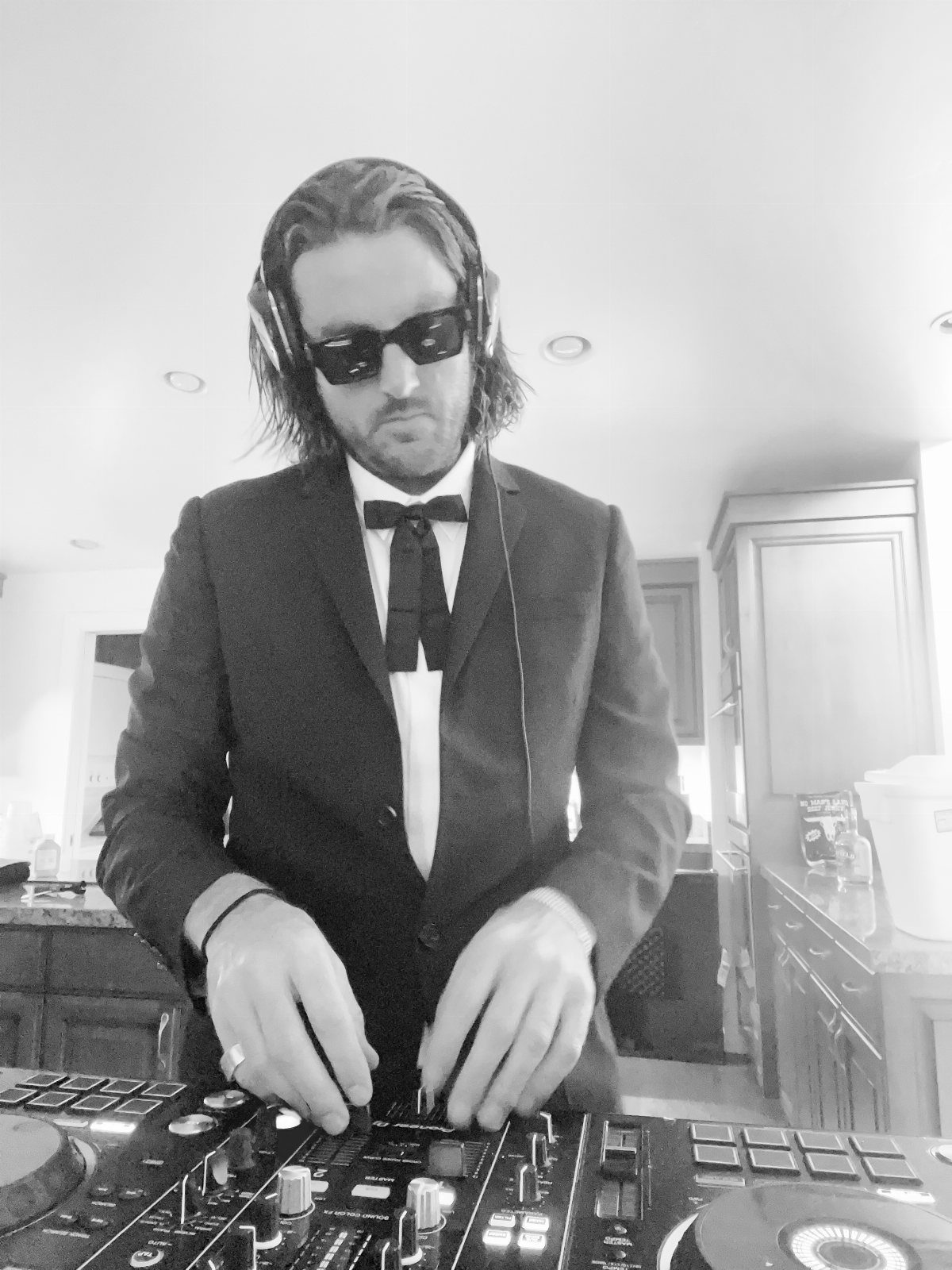 A DJ in a suit and sunglasses operating a professional mixing controller.