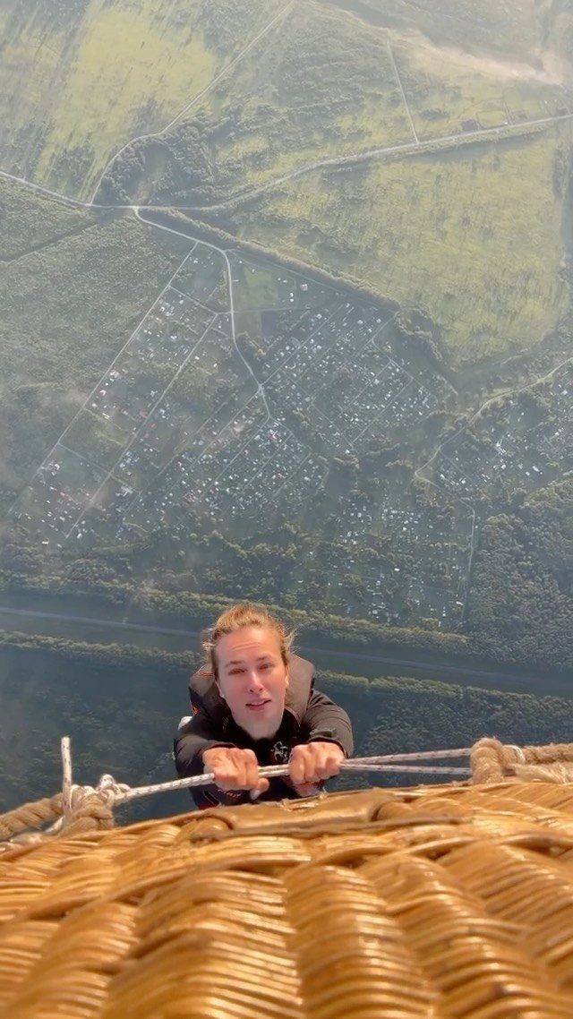 A person looking down from a hot air balloon basket over green fields.