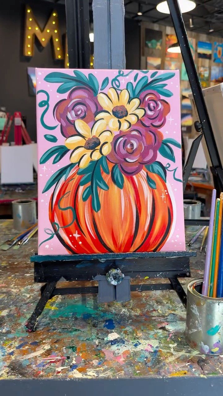 A vibrant floral pumpkin painting displayed on a black easel in an art studio.