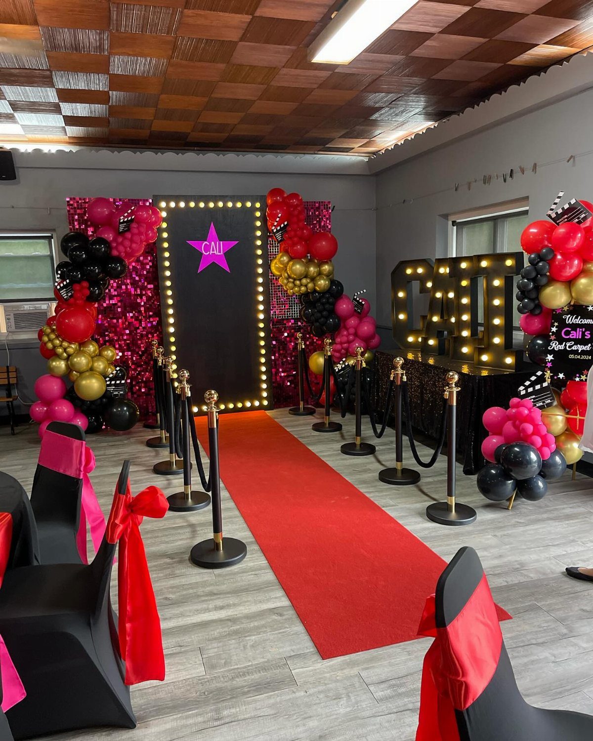 A red carpet walkway lined with gold stanchions and black velvet ropes leading to a decorated entrance.
