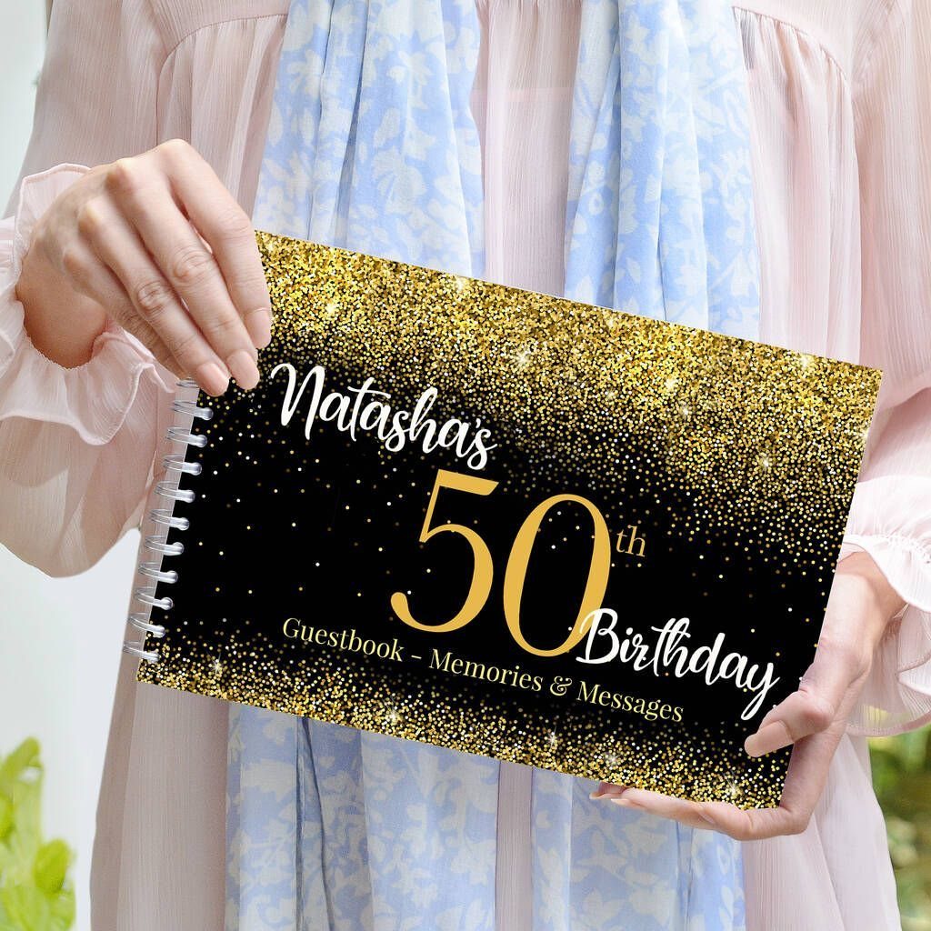 A person holding a black and gold glittery 50th birthday guestbook with white text.