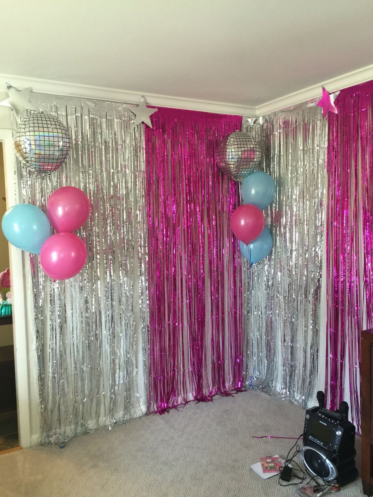 Silver and pink tinsel curtains decorated with disco balls and colorful balloons in a room.