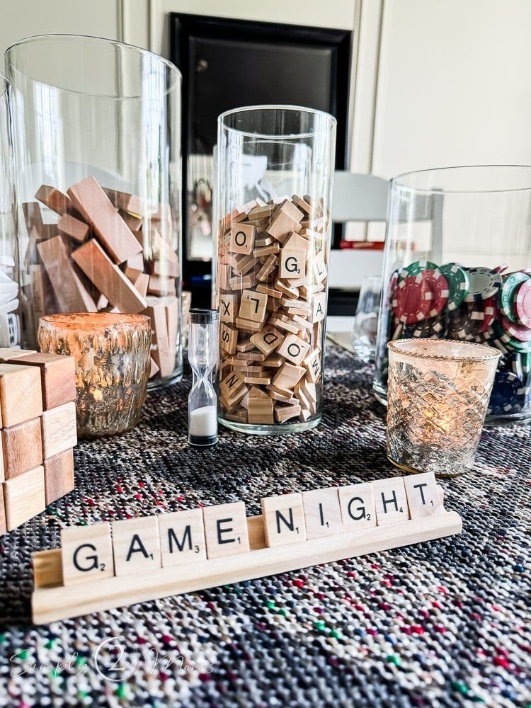 Game night setup with glass vases containing wooden tiles and poker chips on a textured surface.
