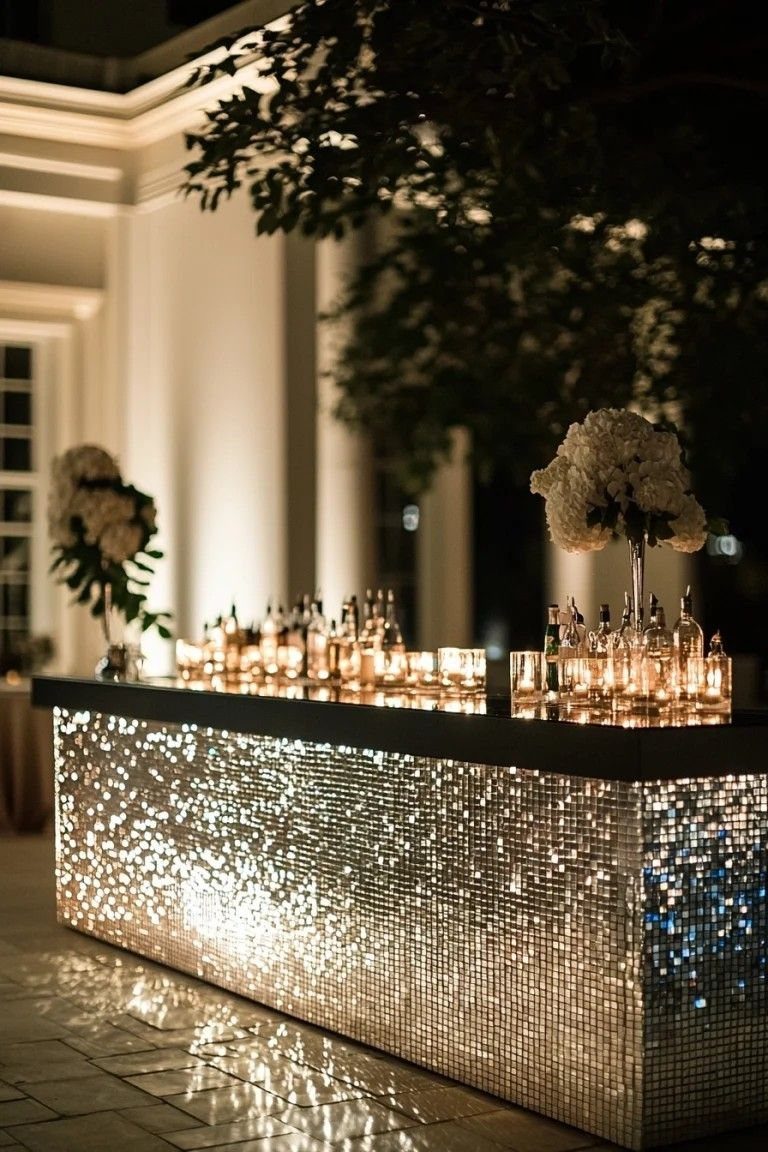 A shimmering gold mosaic bar decorated with glowing candles and white flowers at an evening event.