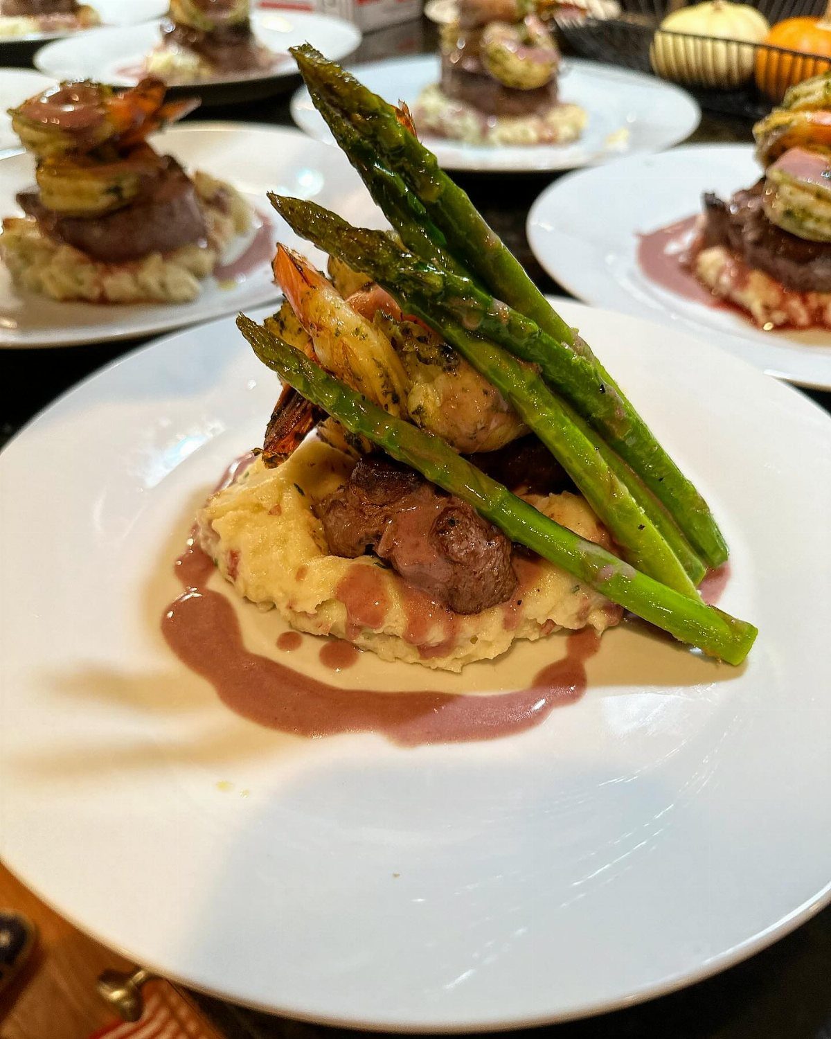 Gourmet plated steak, shrimp, and asparagus served over creamy mashed potatoes on a white plate.