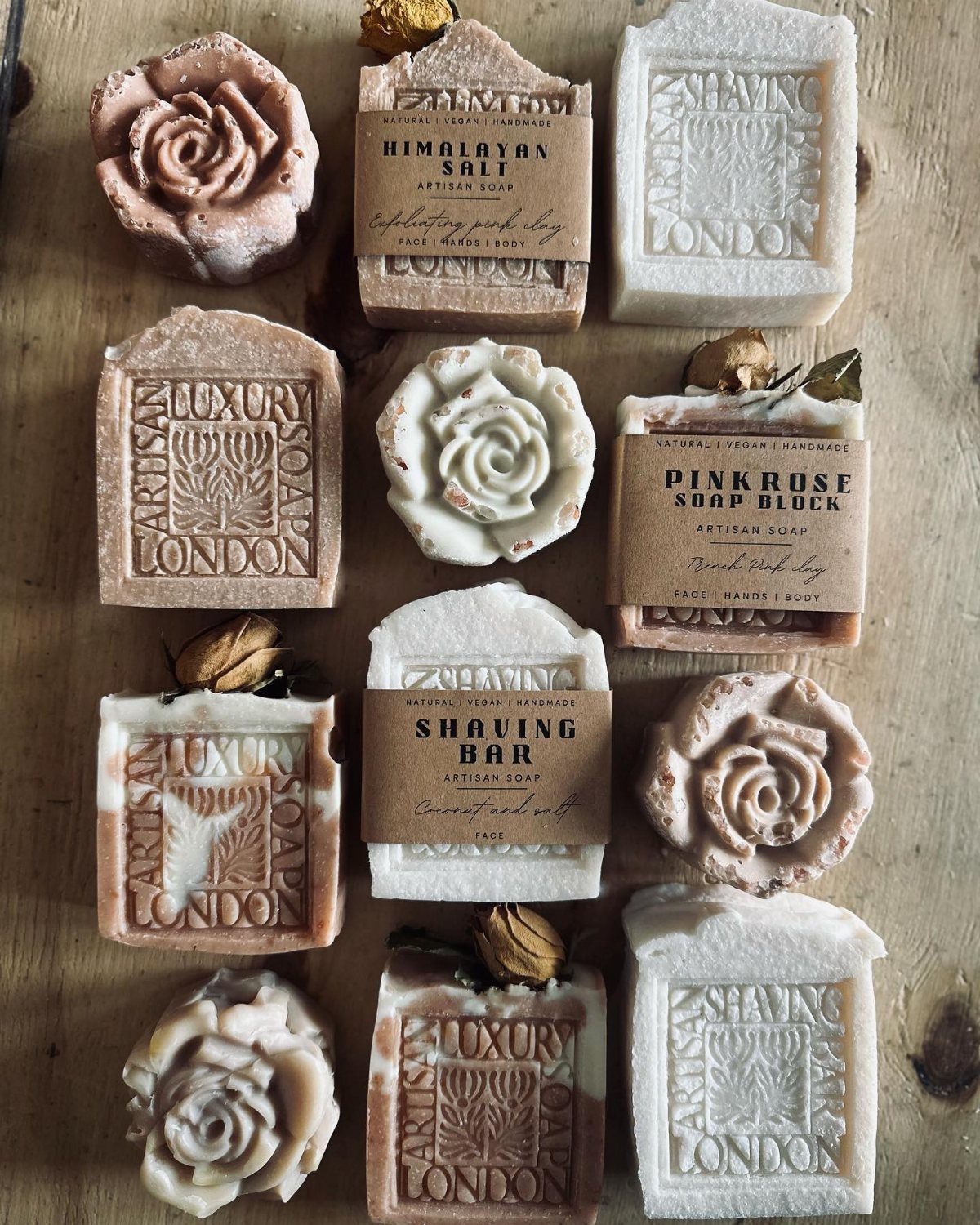 Assorted handmade artisan soap bars in rose shapes and embossed rectangular blocks on wood.