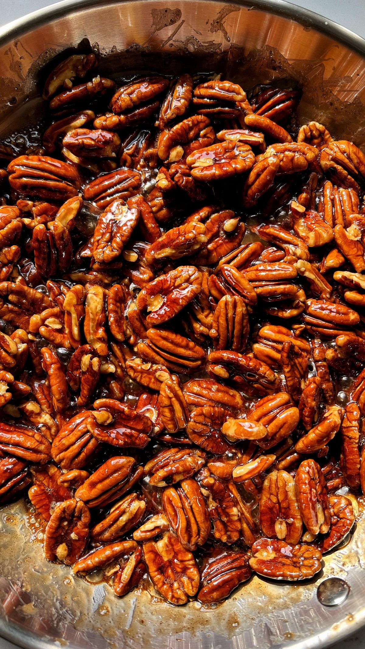 Glazed candied pecans cooking in a shiny stainless steel pan.