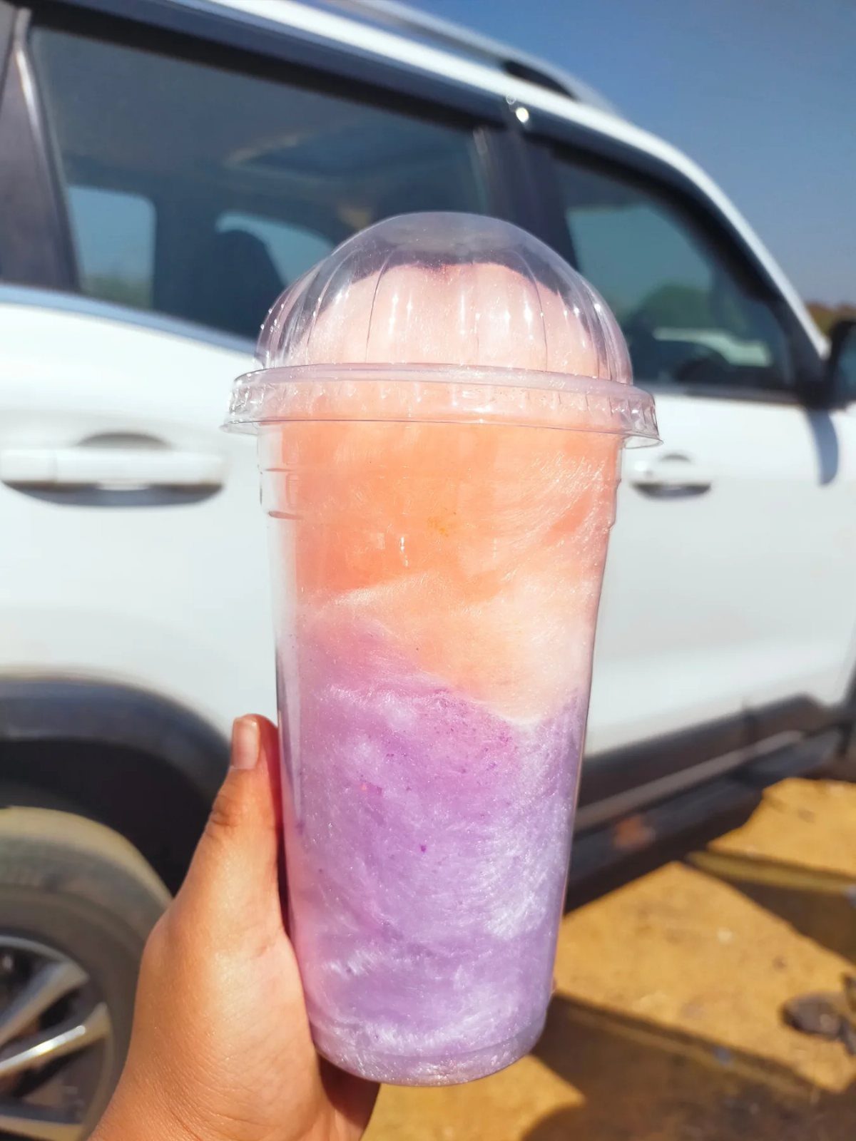A hand holding a clear plastic cup filled with pink and purple cotton candy.
