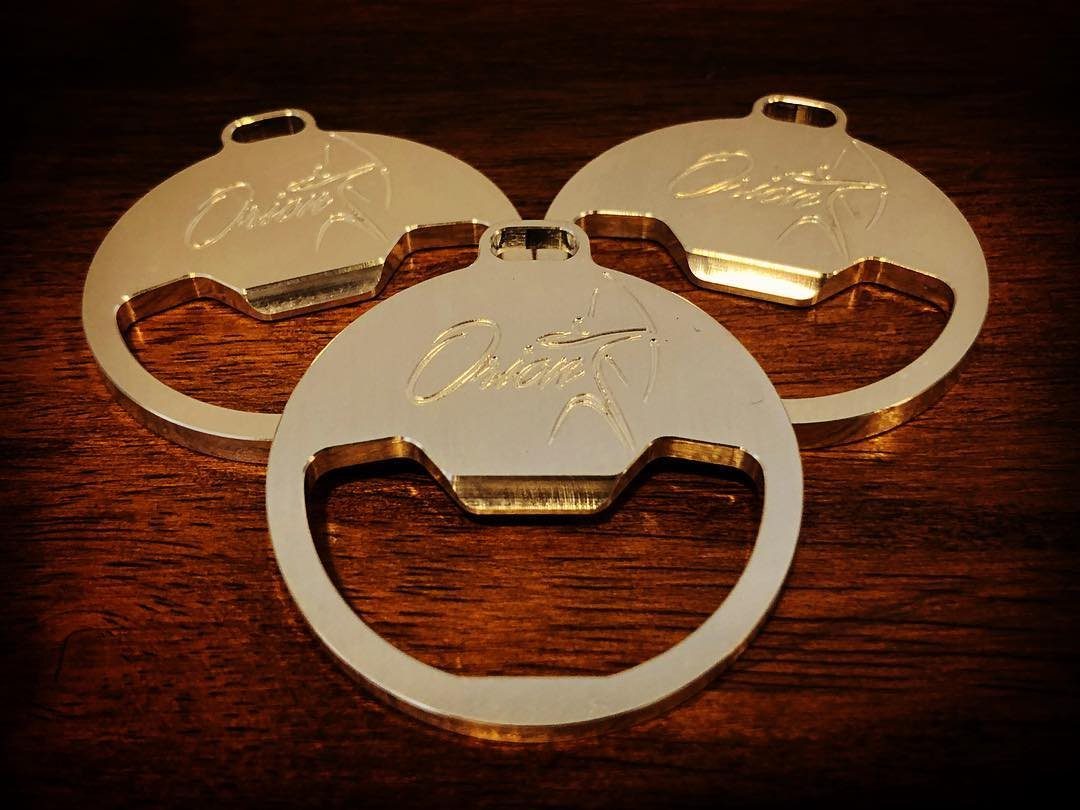 Three gold engraved metal bottle openers resting on a dark wooden tabletop.