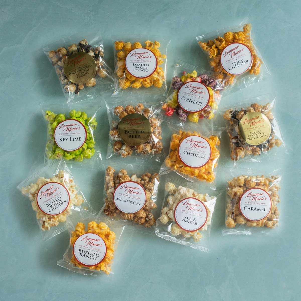 Various small clear bags of flavored gourmet popcorn arranged on a light blue background.