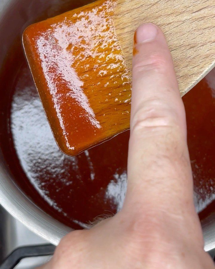 A wooden spatula coated in thick reddish-brown BBQ sauce inside a metal pot.