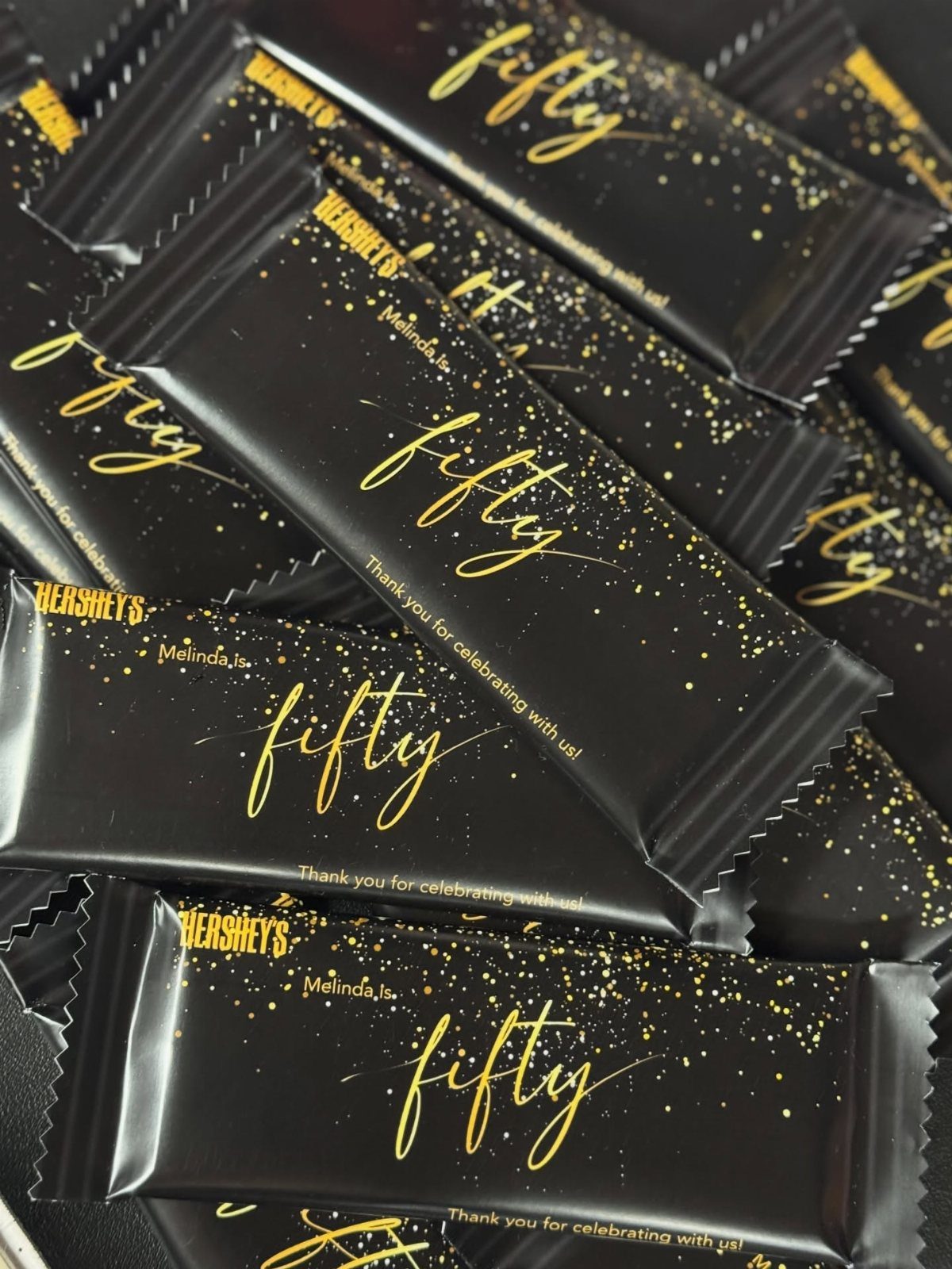 Black chocolate candy bars with gold glitter and fifty birthday text on wrappers.