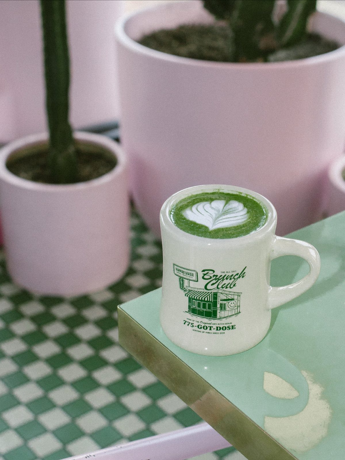 A white mug of matcha latte with heart latte art on a teal table.