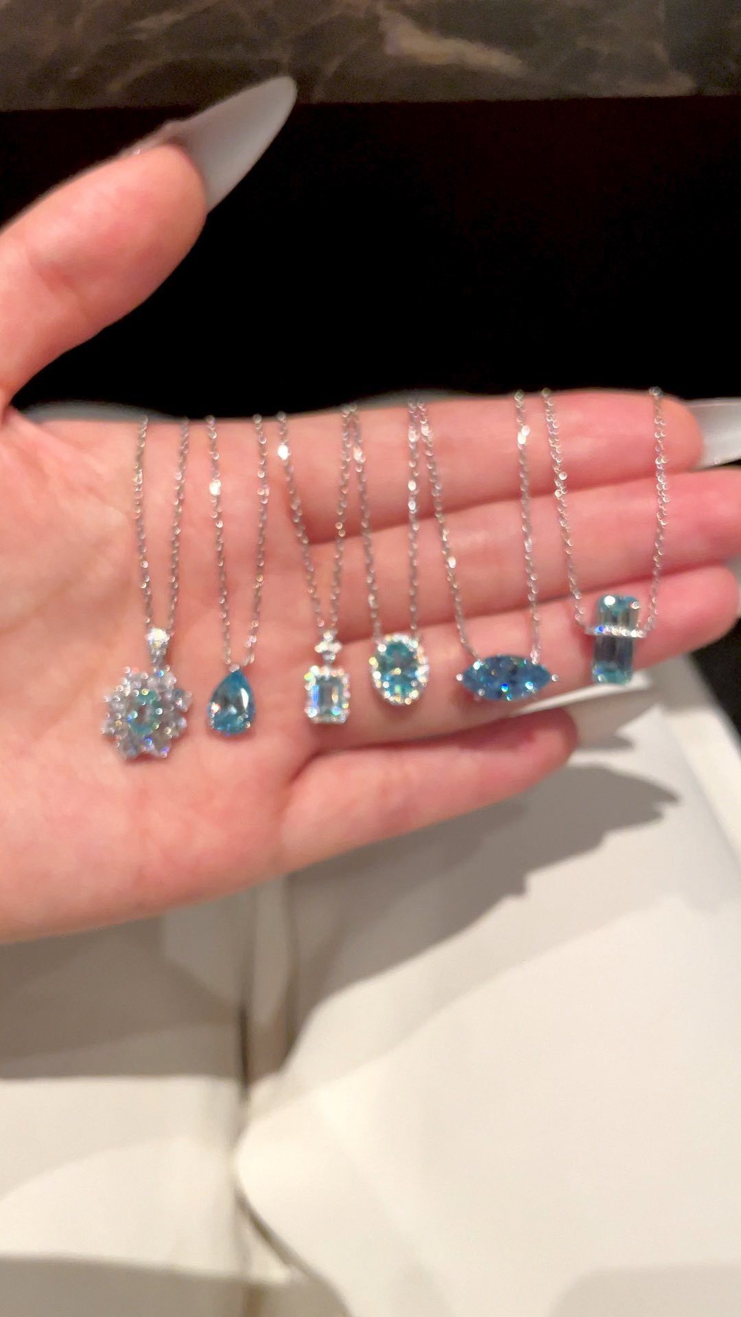 Seven silver necklaces with light blue gemstone pendants held in a person's hand.