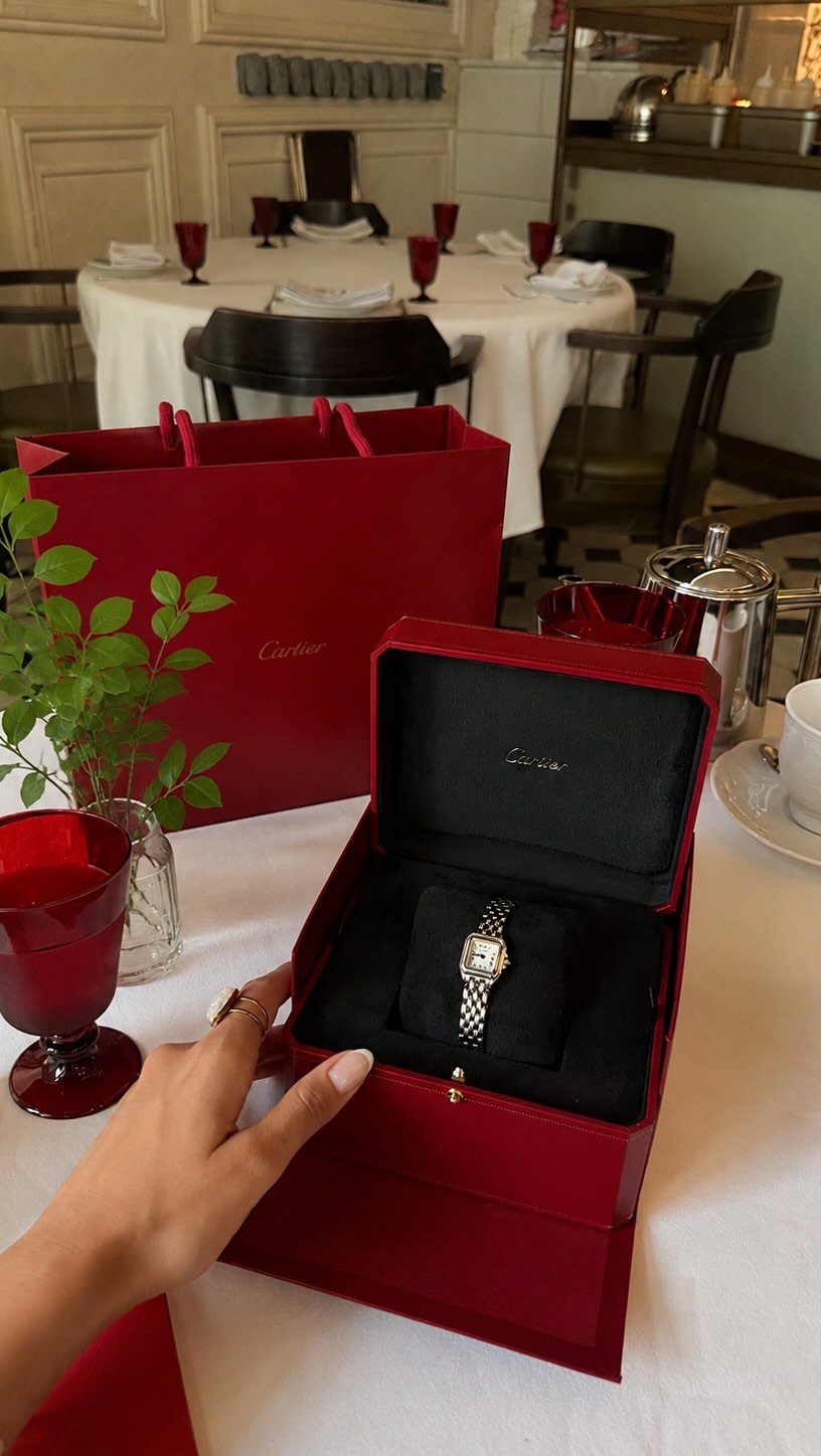 A silver and gold watch inside an open red luxury gift box on a table.