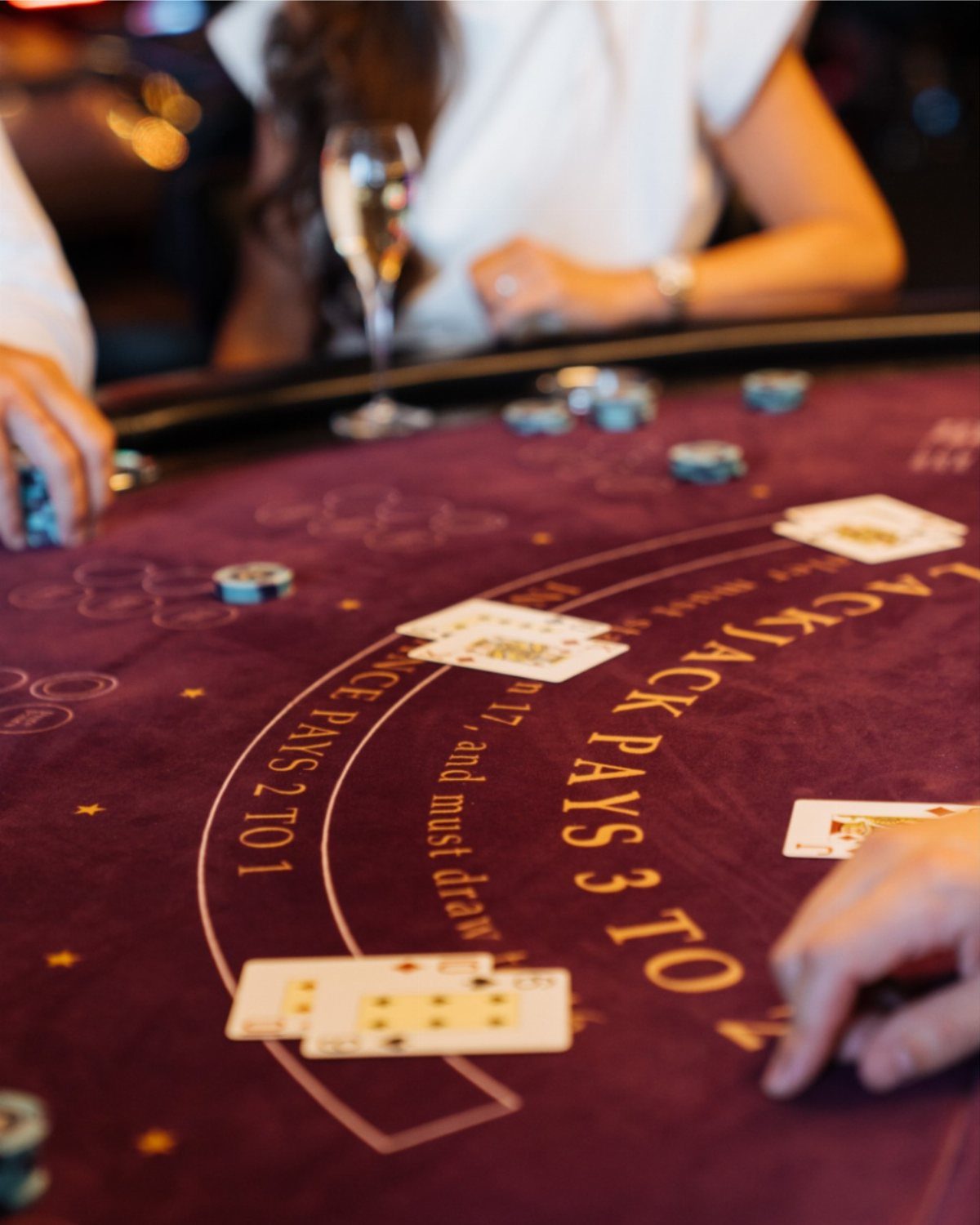 Blackjack cards and gambling chips on a maroon casino table with hands playing.
