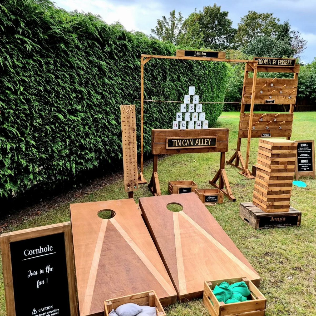 Wooden lawn games including cornhole and tin can alley set up on a grassy lawn.