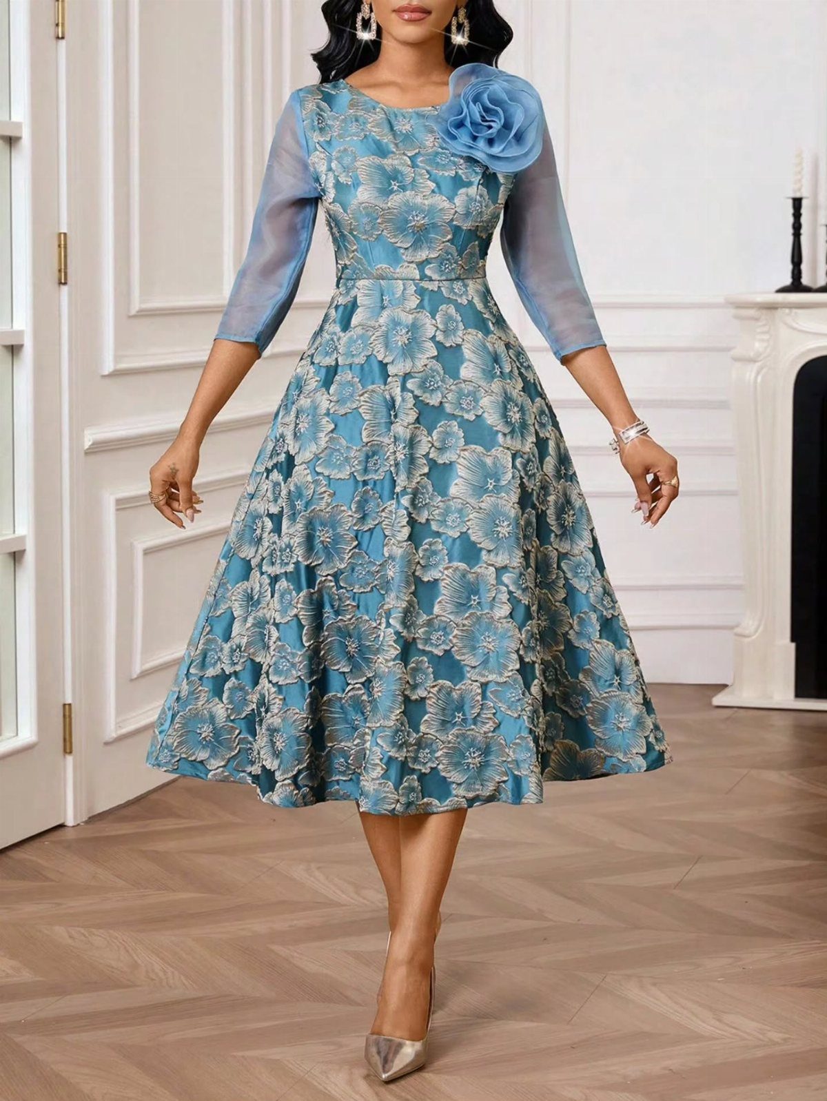 Woman posing in a teal and gold floral fit-and-flare midi dress with a shoulder rose.