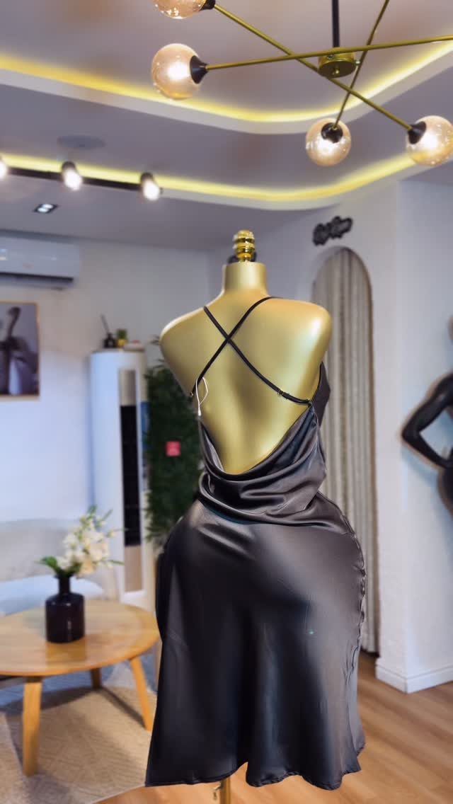 Black satin slip dress with thin criss-cross straps displayed on a gold mannequin.