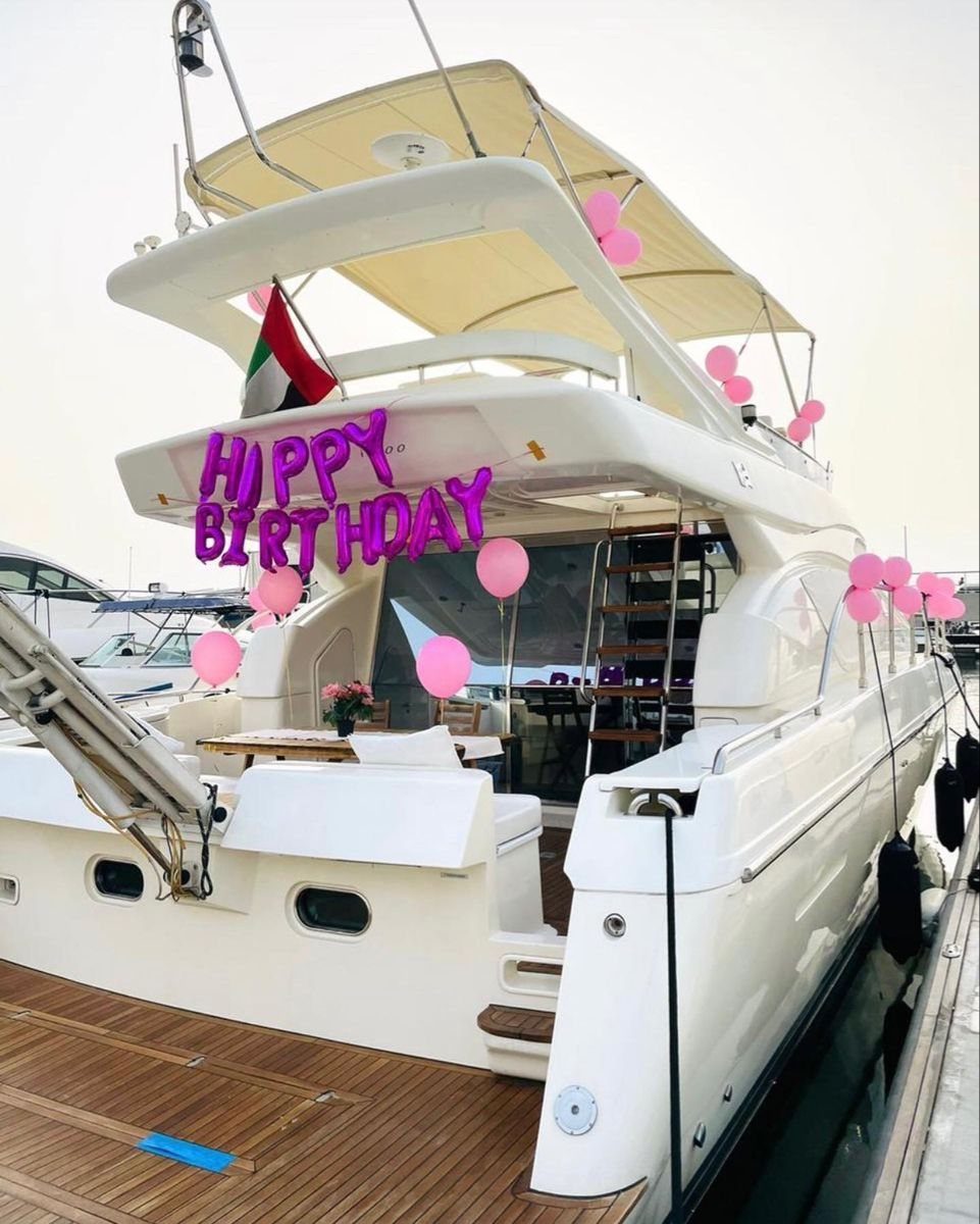 A white luxury yacht decorated with pink balloons and happy birthday lettering docked at a pier.
