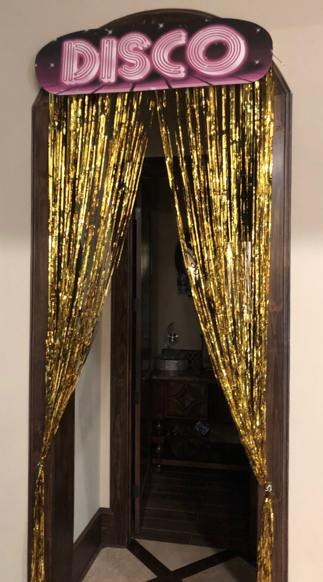 Gold tinsel curtains frame a doorway topped with a pink disco sign.