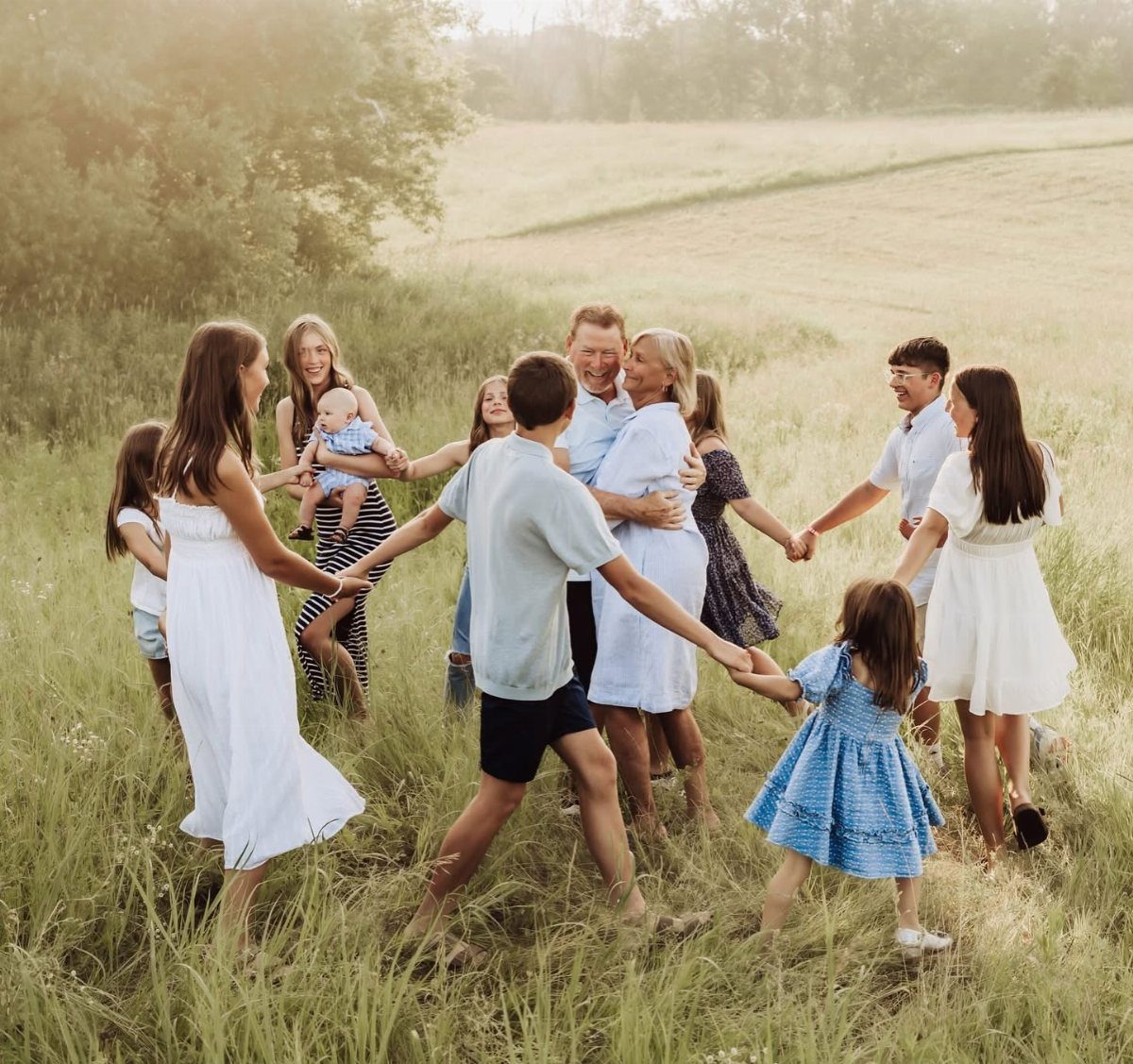 A multi-generational family holding hands in a circle in a sunny grassy field.