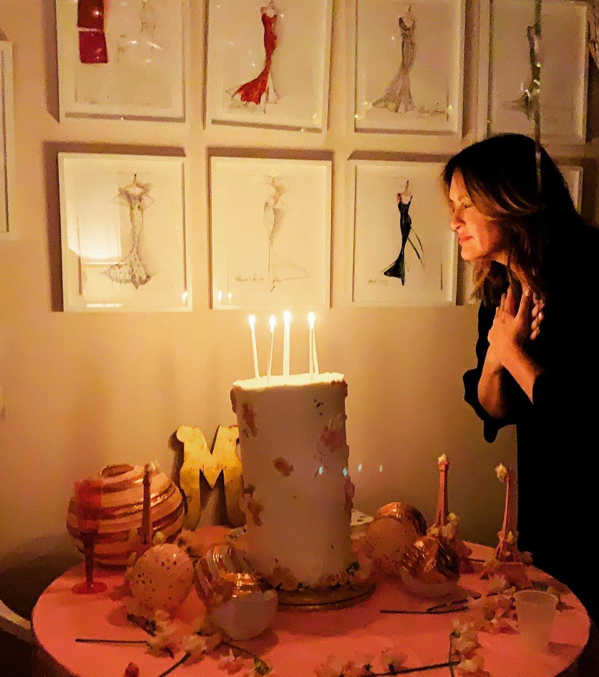 A woman leaning toward a white birthday cake with lit candles on a pink table.