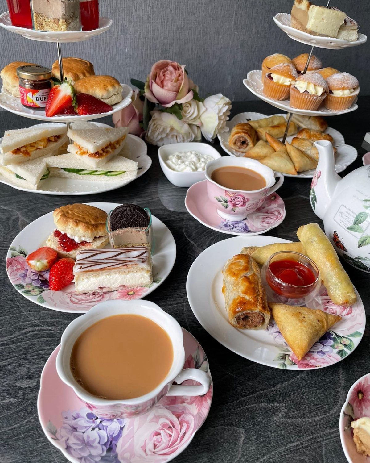 Afternoon tea spread with finger sandwiches, scones, pastries, and tea in floral cups.